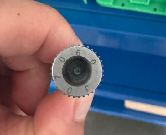 A metal print wheel photographed in hand — characters 0, 9, 0, 6, 0 and J are stamped around the rim.